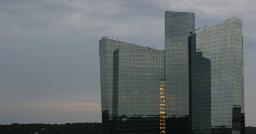 Modern glass skyscraper reflecting the sky, with a few lit windows, set against a cloudy backdrop.
