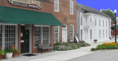Exterior view of the Ford W. Long Museum, featuring a green awning, benches, and flower beds along a sidewalk.