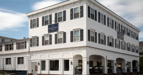 A white, three-story building with black shutters and signs reading "The Whalers Inn" on a sunny day.