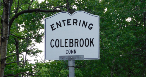 Sign reading "Entering Colebrook Conn" surrounded by green trees.