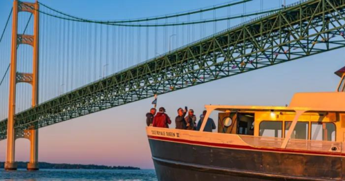 A boat near a bridge at sunset, with people on board enjoying the view.