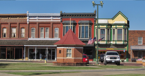 Historic buildings line a street, featuring brick facades and colorful architecture, with a small gazebo in the foreground.