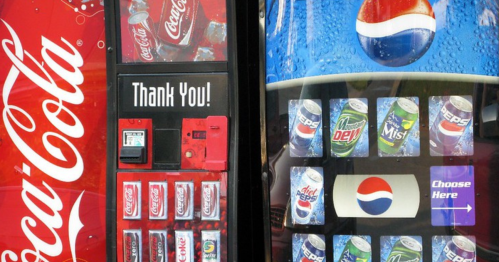 A side-by-side view of Coca-Cola and Pepsi vending machines with various drink options displayed.