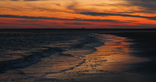 A serene beach at sunset, with waves gently lapping at the shore and vibrant orange and purple hues in the sky.