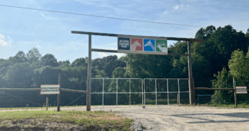 Entrance gate with signs for clean water, nature, and wildlife, surrounded by trees and a gravel path.
