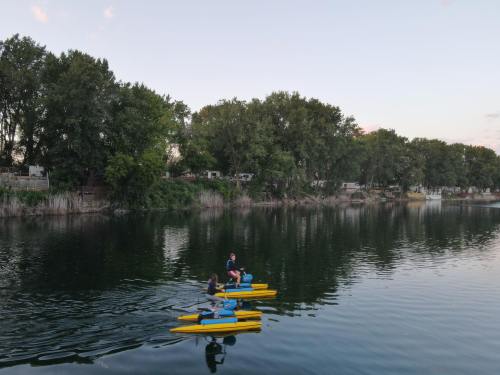 Two people kayak on a calm river surrounded by trees and reflections in the water during sunset.