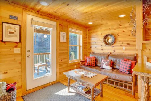 Cozy wooden interior with a leather sofa, plaid pillows, and a door leading to a deck, surrounded by natural light.