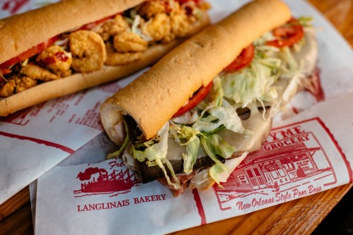 Two New Orleans-style po' boy sandwiches on paper, one filled with fried shrimp and the other with lettuce, tomatoes, and meats.