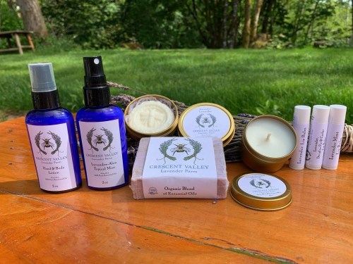 A collection of natural skincare products on a wooden table, including sprays, balms, candles, and lip balms.