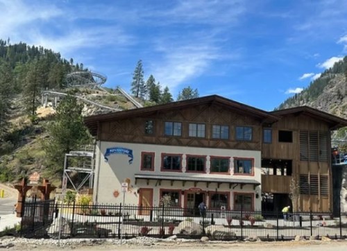 A mountain-themed building with a wooden facade, surrounded by trees and hills, under a clear blue sky.