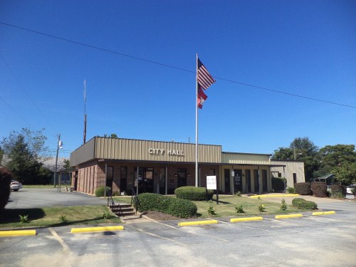 City Hall building with an American flag, surrounded by greenery and a clear blue sky.