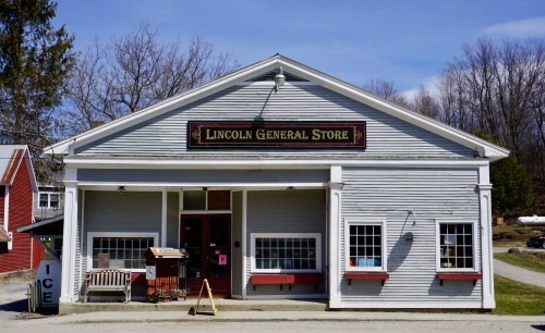 Front view of the Lincoln General Store, featuring a sign, large windows, and a porch with seating.