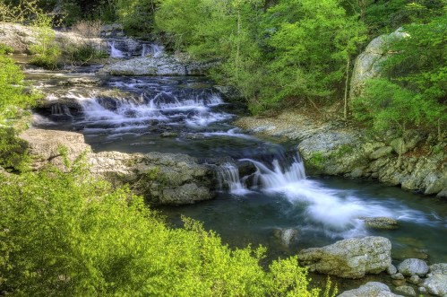 A serene stream flows through lush greenery, with gentle waterfalls cascading over rocky formations.