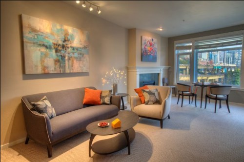 A modern living room with a gray sofa, light-colored chair, coffee table, and colorful artwork on the walls.