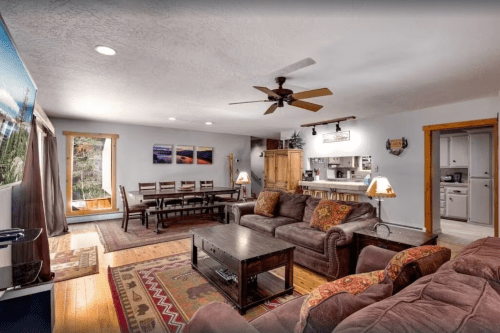 Cozy living room with a large sofa, dining table, and kitchen area, featuring warm lighting and rustic decor.