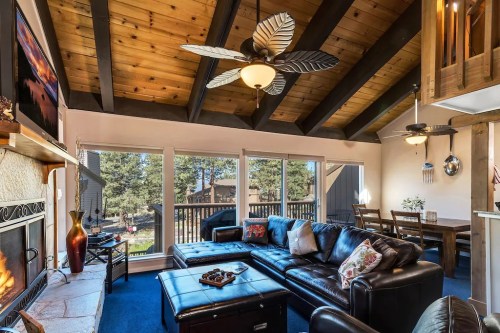 Cozy living room with wooden beams, leather furniture, and large windows overlooking a forested area.