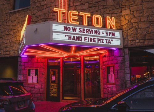 Neon-lit entrance of Teton restaurant with a marquee announcing "Hand Fire Pizza" and a serving time of 5 PM.