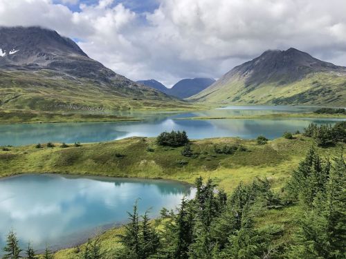 A serene landscape featuring turquoise lakes surrounded by lush greenery and mountains under a partly cloudy sky.