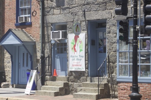 A stone building with a blue door and a sign for "Matsu Time Gift Shop" featuring Japanese gifts and snacks.