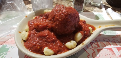 A dish of meatballs in marinara sauce served over gnocchi, presented in a white oval bowl.