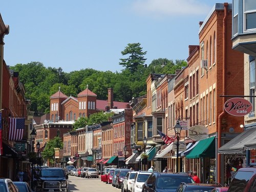 A charming street lined with historic brick buildings, shops, and trees under a clear blue sky.