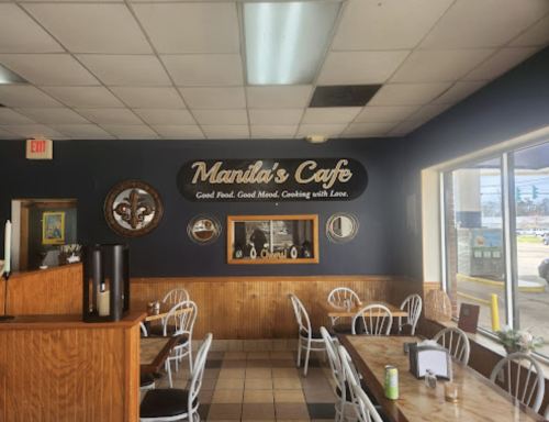 Interior of Manila's Cafe featuring wooden decor, tables, and a wall sign that reads "Good Food. Good Mood. Cooking with Love."