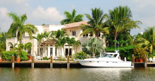 A white waterfront mansion on a canal near a dock and a boat