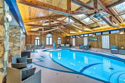 Indoor swimming pool area with wooden beams, skylights, and seating around the pool. Relaxing and spacious atmosphere.
