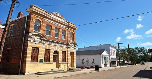 Historic brick building with decorative facade, surrounded by a quiet street and blue sky.