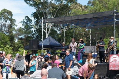A lively outdoor music event with a band performing on stage and an audience dancing and enjoying the atmosphere.
