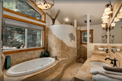 Spacious bathroom with a curved stone wall, large tub, dual sinks, and natural light from a large window.