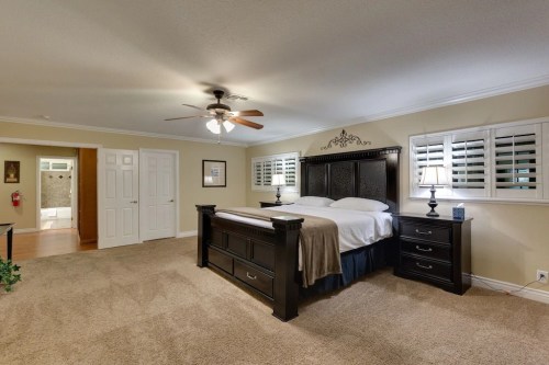 Spacious bedroom with a large bed, nightstands, ceiling fan, and light-colored walls. Doorway leads to a bathroom.