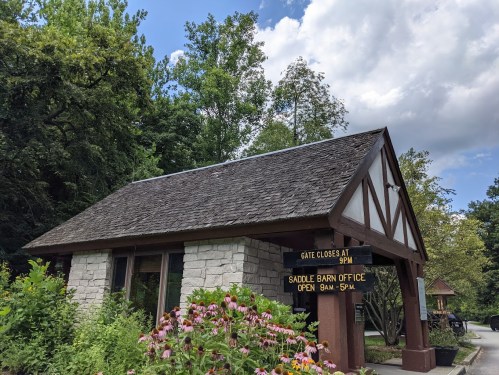 A small stone and wood building surrounded by greenery, with signs indicating office hours and gate closing time.