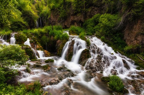 A serene waterfall cascades over rocky terrain, surrounded by lush greenery and vibrant foliage.