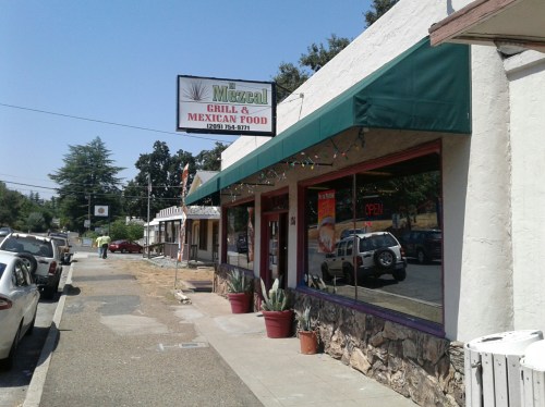 A street view of a Mexican restaurant with a green awning, sign, and parked cars along the sidewalk.