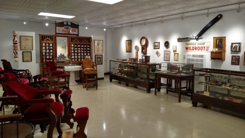 A vintage barber shop interior featuring antique chairs, memorabilia, and display cases filled with barber tools.