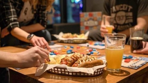 A group enjoys snacks and drinks while playing a board game at a table in a lively setting.