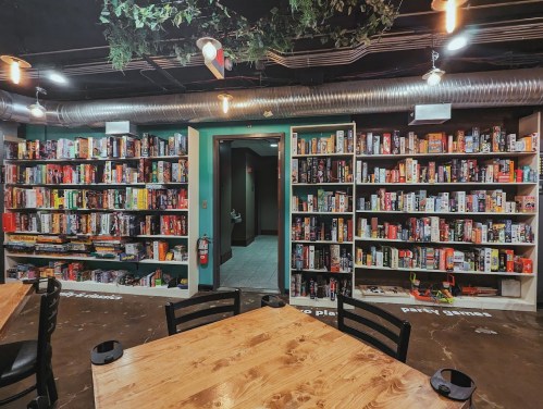 A cozy game room with shelves filled with board games, wooden tables, and soft lighting.