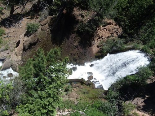 Aerial view of a cascading waterfall surrounded by lush greenery and rocky terrain.