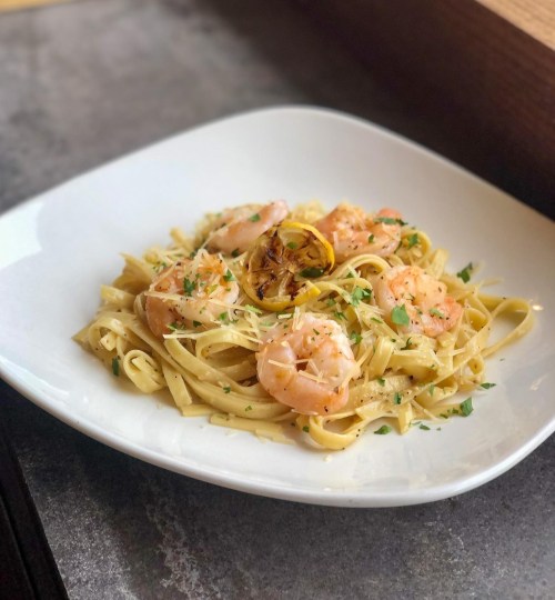 A plate of fettuccine pasta topped with shrimp, lemon, and herbs, served in a white bowl.