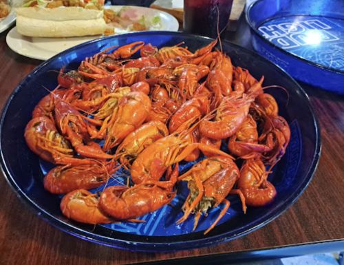 A blue plate filled with bright red crawfish, served on a wooden table with food in the background.