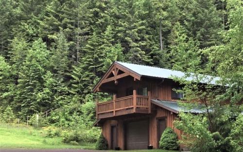 A wooden cabin with a balcony surrounded by lush green trees in a forested area.
