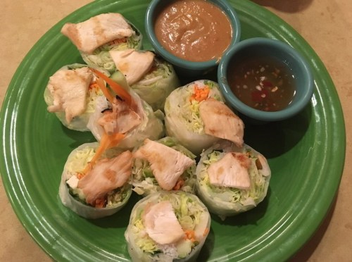 Fresh spring rolls with chicken, served with peanut sauce and a tangy dipping sauce on a green plate.