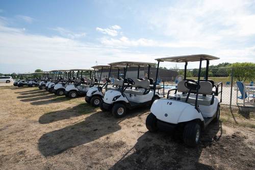 A row of white golf carts parked on a dirt lot under a clear blue sky.