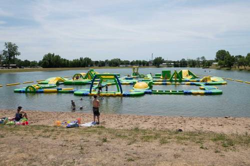 A colorful inflatable water park on a lake, with people playing and relaxing on the sandy shore.