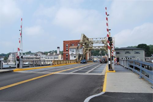 A drawbridge with raised barriers, allowing vehicles to cross over a waterway, surrounded by buildings and boats.