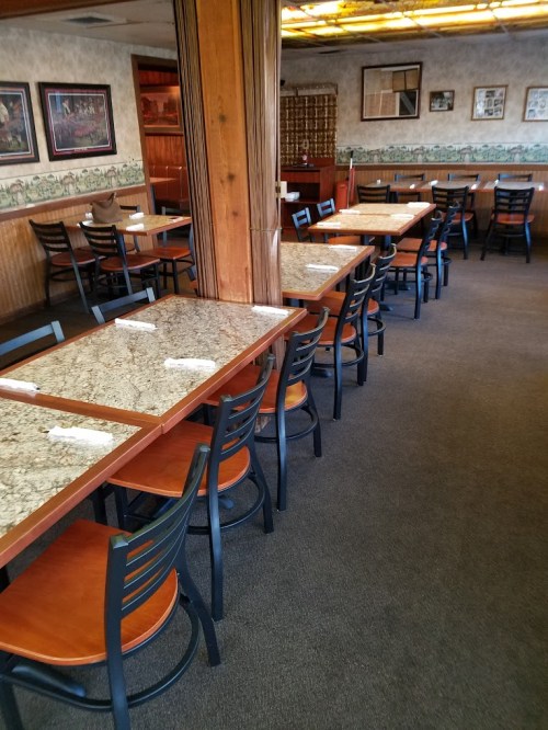 Interior of a restaurant featuring empty tables and chairs, with wooden accents and a cozy atmosphere.