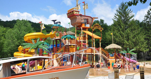 Colorful water park with a pirate ship structure, slides, and palm trees, bustling with families enjoying the sun.
