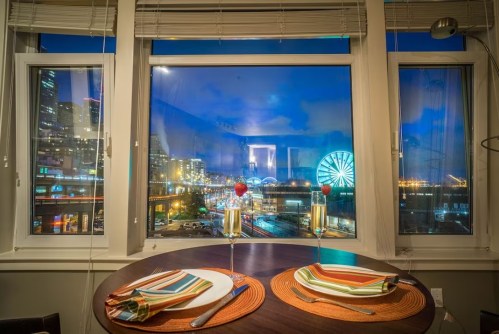 A cozy dining table set for two, with a view of a city skyline and a ferris wheel at night.