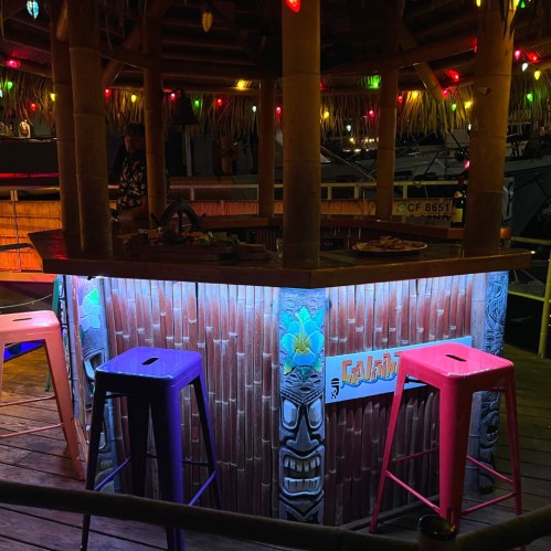 A tiki bar with colorful lights and stools, featuring a carved tiki design on the counter.